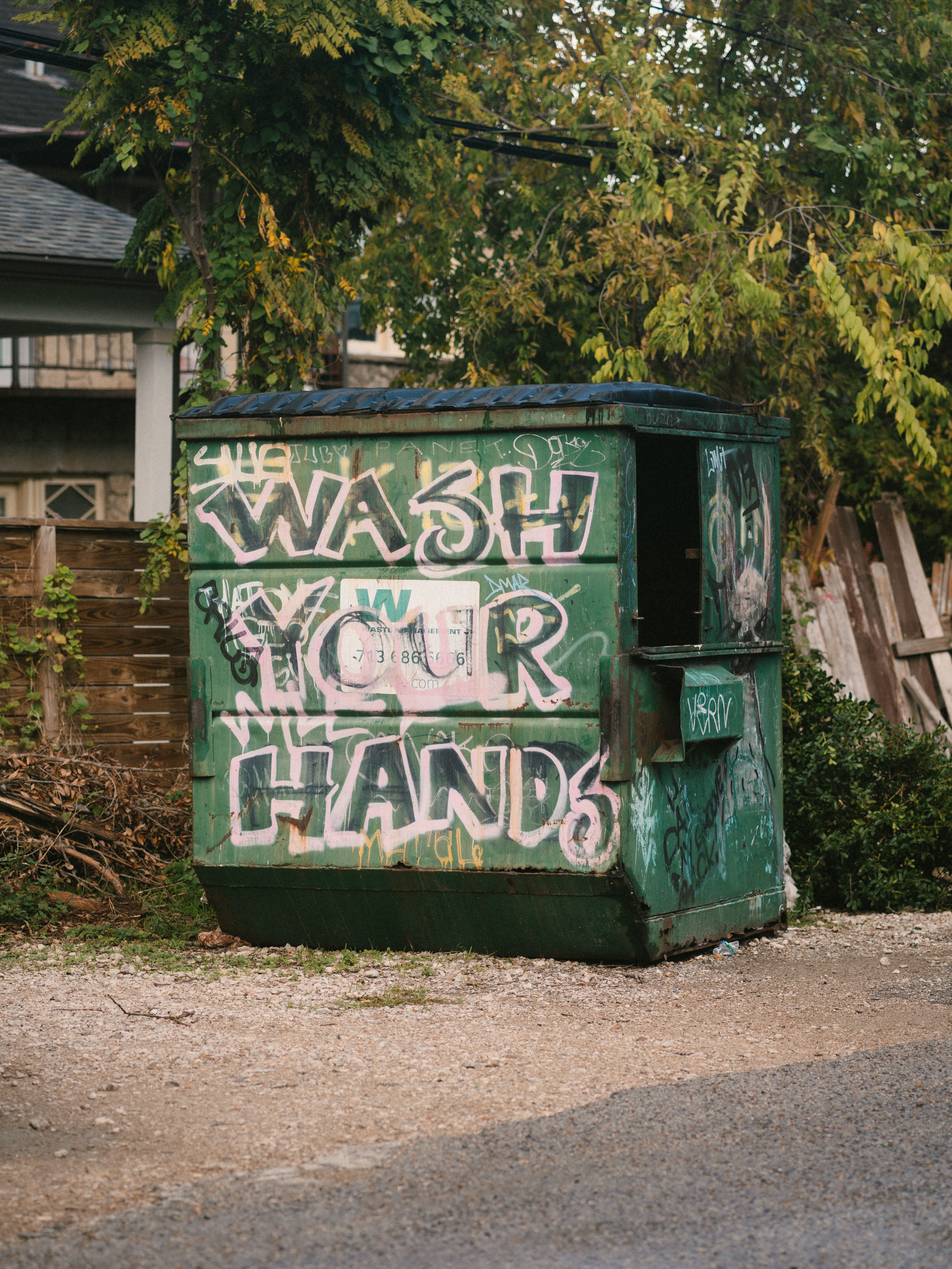 Graffiti on a green dumpster reads 'Wash Your Hands' in an urban setting.