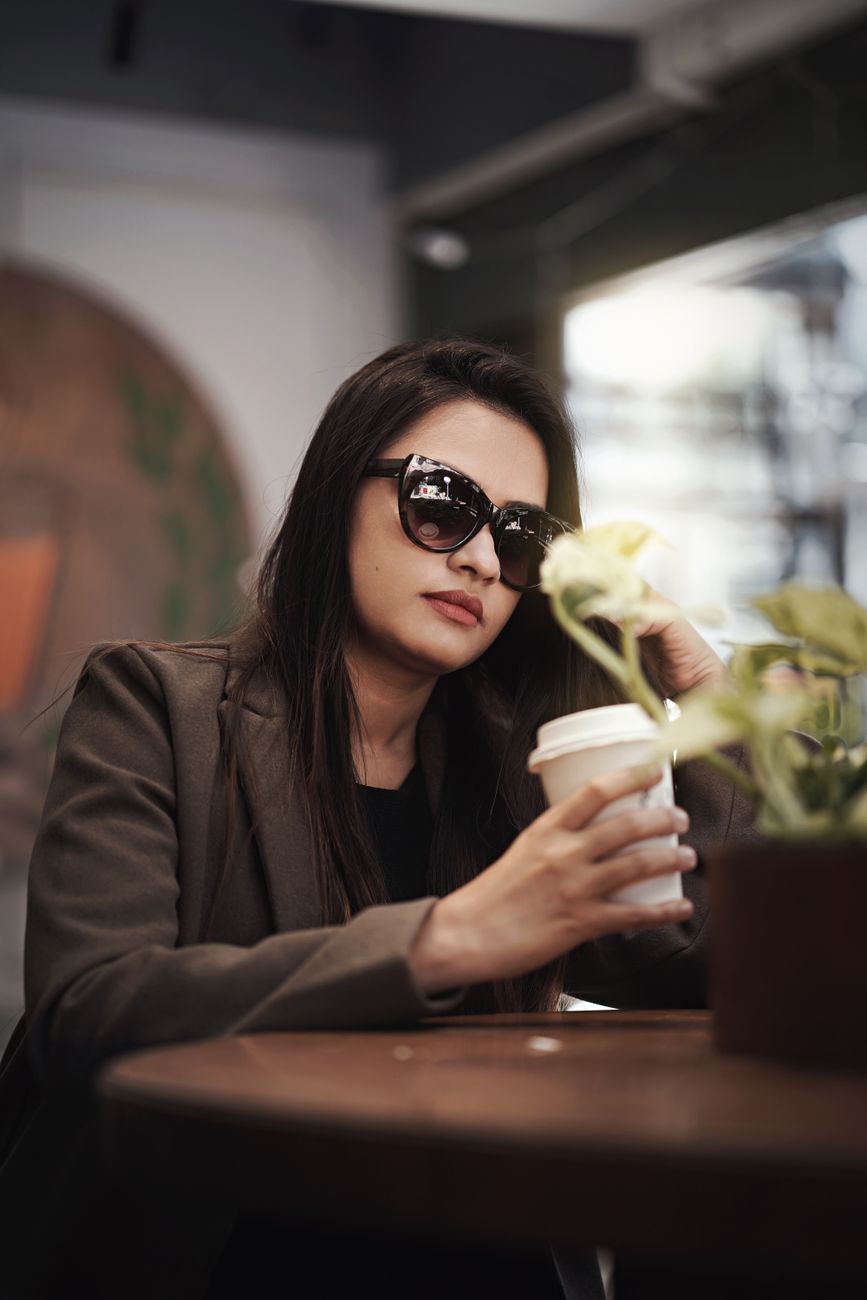Woman in sunglasses enjoys coffee indoors, creating a modern, casual vibe.