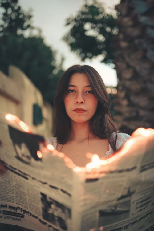 Free A young woman holds a burning newspaper outdoors, creating an artistic and dramatic scene. Stock Photo