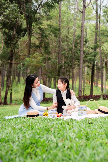 Mẹ Bầu Ăn Macca Việt Nam Được Không? Nên Ăn Bao Nhiêu Là Tốt Nhất? 4 A mother and daughter enjoy a sunny picnic in a lush forest setting with snacks and toys.
