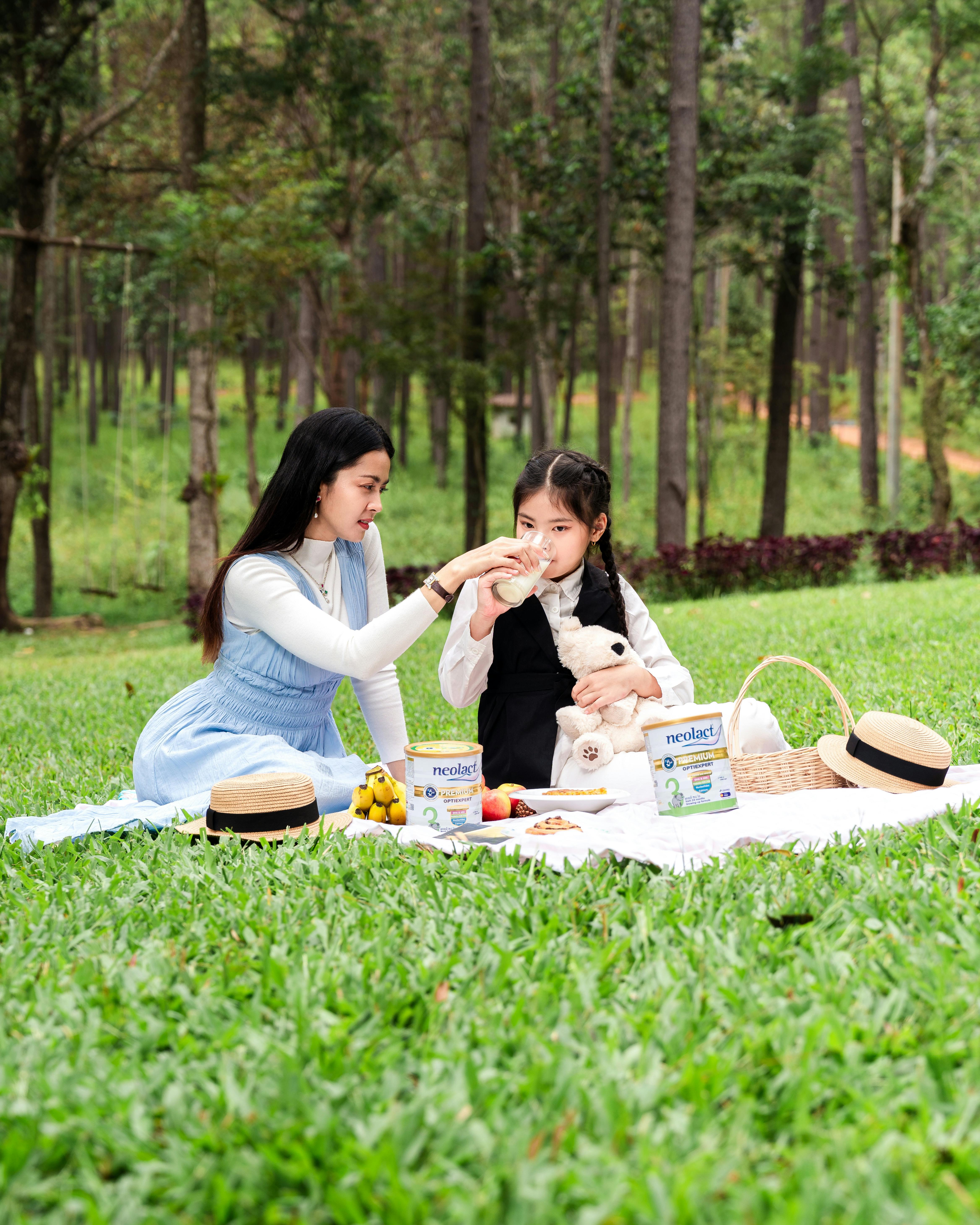 Mother and daughter sharing a picnic in a lush park, enjoying quality time together under the trees.