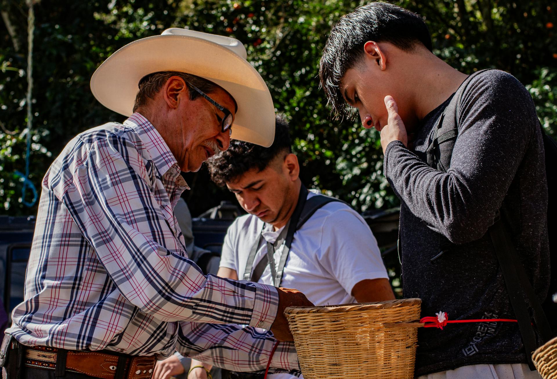 Three men in discussion over a basket at an outdoor market, focusing on trade or negotiation.