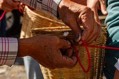 Detailed image of hands weaving a basket with red rope outdoors, showcasing traditional craftsmanship.