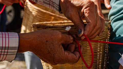 Detailed image of hands weaving a basket with red rope outdoors, showcasing traditional craftsmanship.