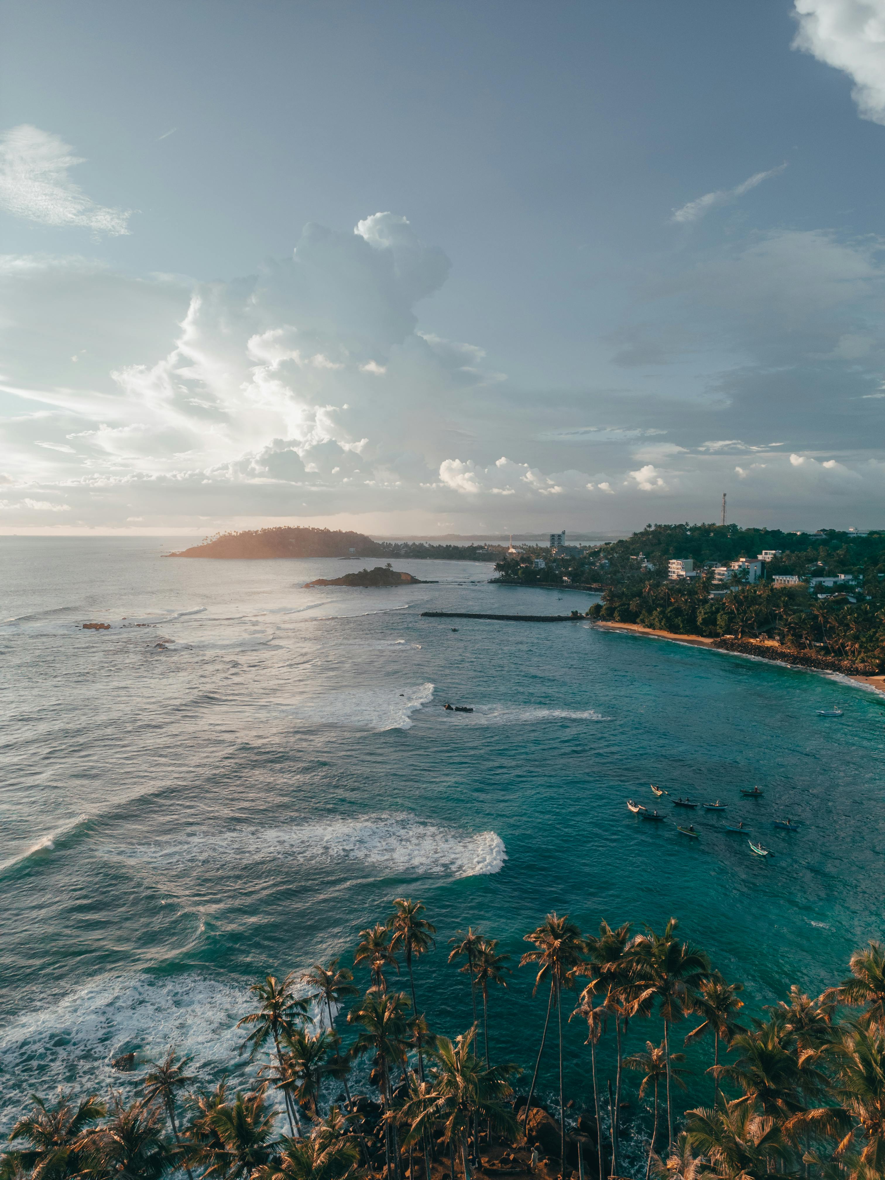 A stunning aerial view of Sri Lanka's coastline with palm trees, clear ocean waves, and a vibrant sunset sky.