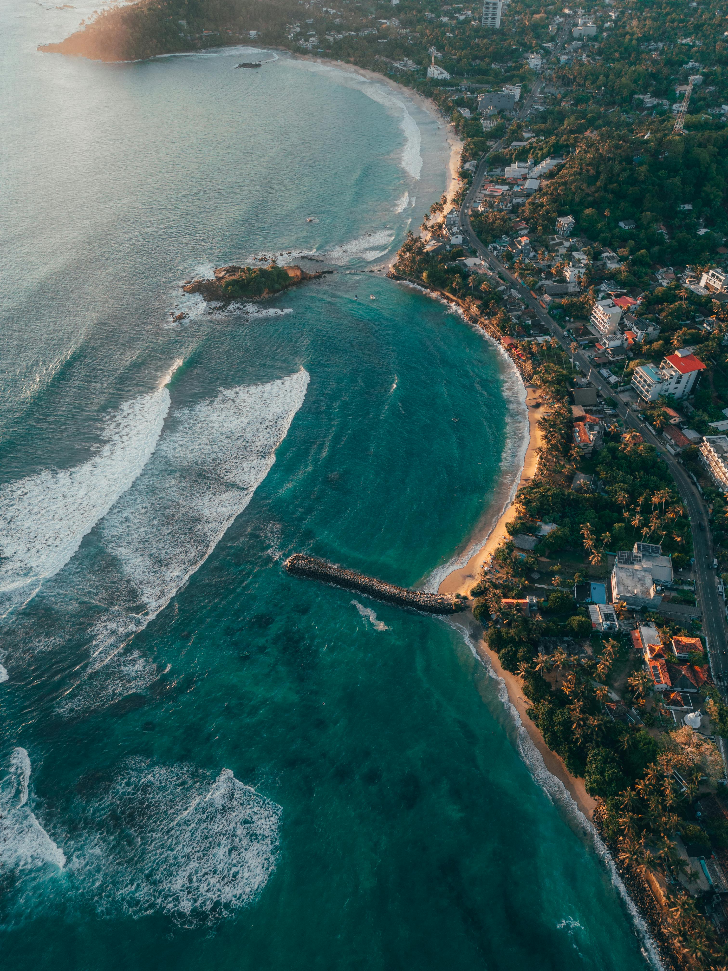 Stunning aerial view of a coastal town in Sri Lanka with vibrant waters and lush greenery at sunset.