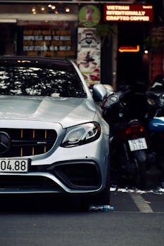 Silver luxury car parked on a busy urban street with motorcycles in background.