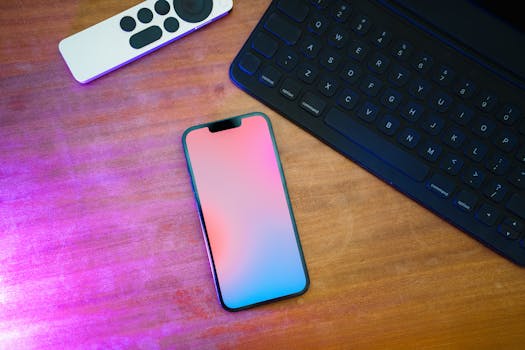 A sleek workspace setup featuring a smartphone, keyboard, and remote on a wooden desk.