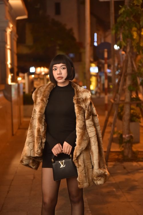 Free Stylish woman in fur coat holding designer bag, city street backdrop. Stock Photo