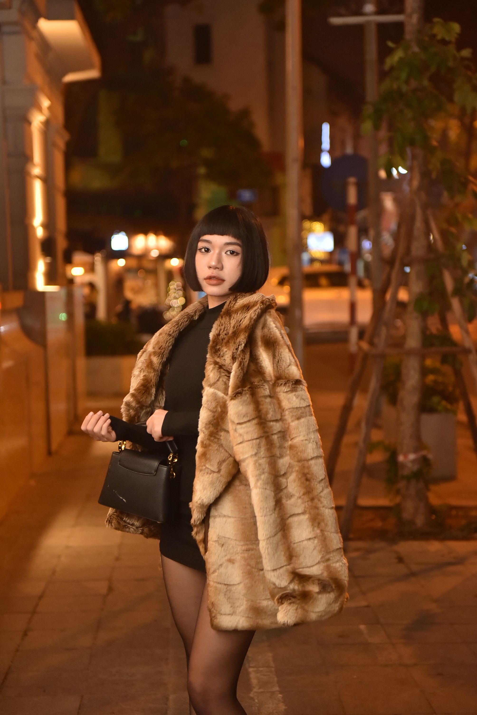 woman in black satin slip dress under a faux fur coat