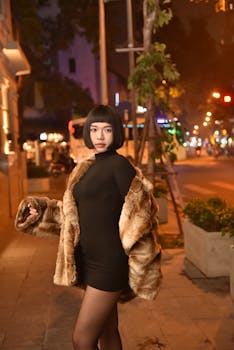 Elegant woman in fur coat poses confidently on a vibrant night city street.