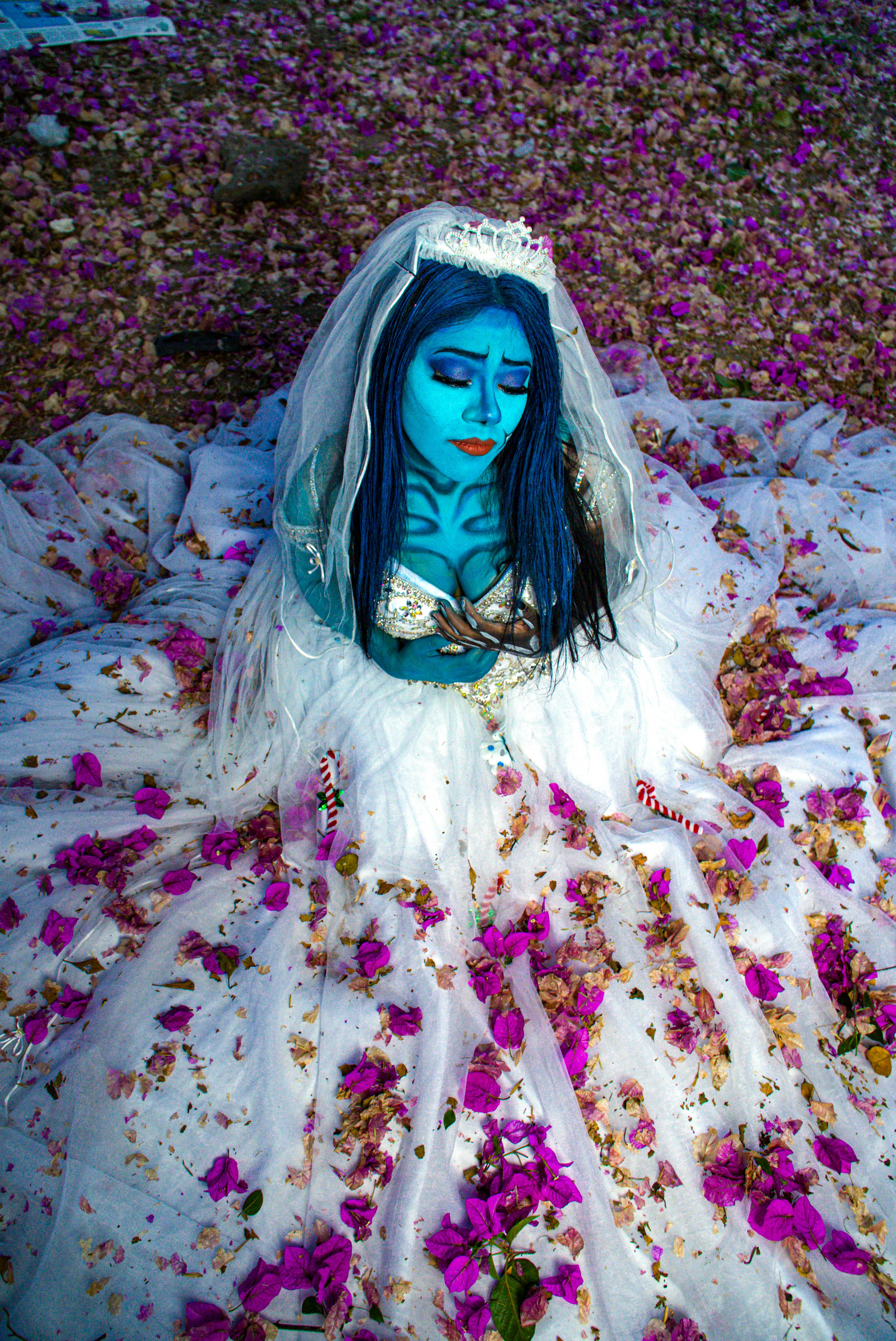 Creative portrait featuring a woman in blue body paint with floral surroundings and a white gown.