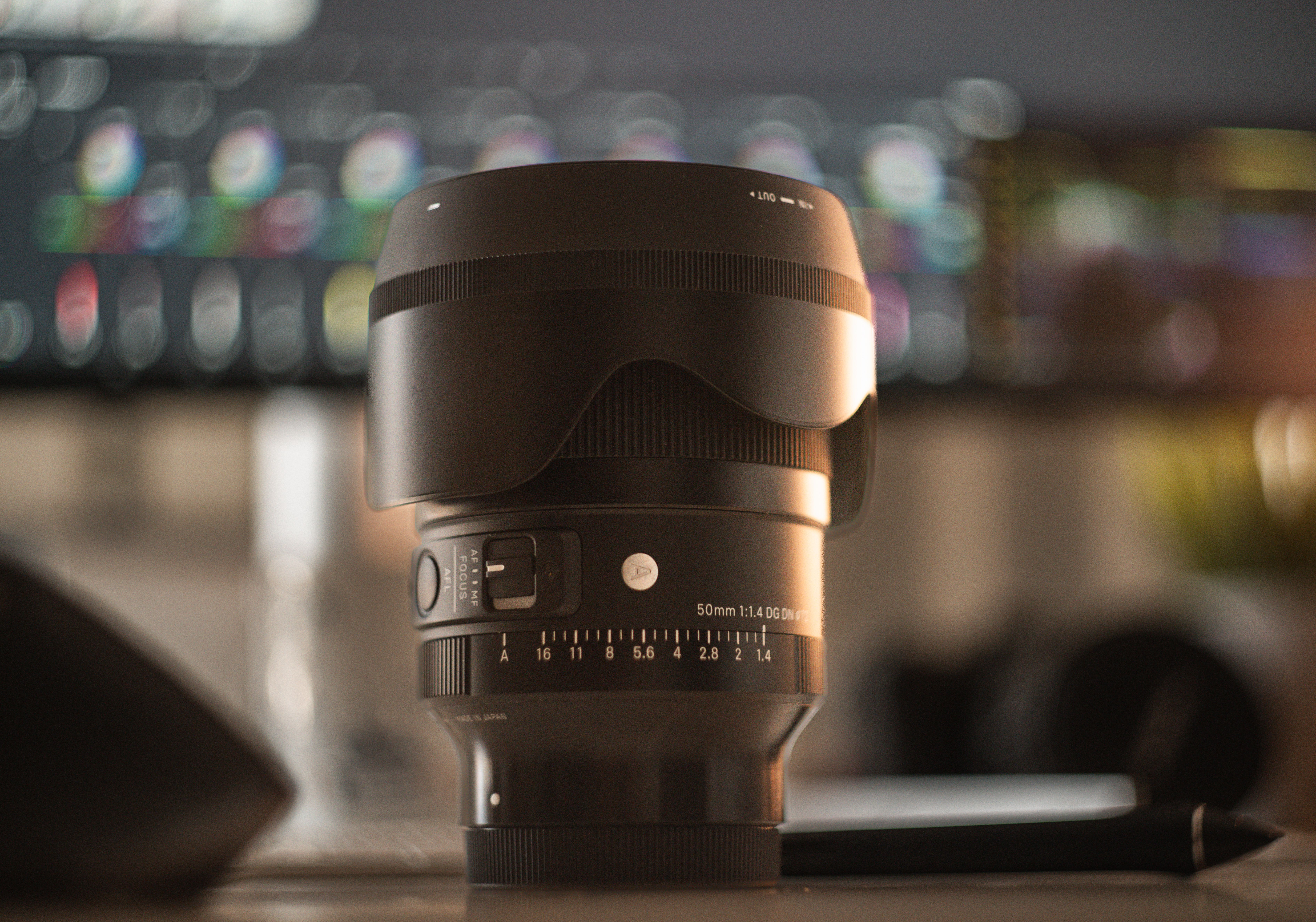 Vista dettagliata di un obiettivo fotografico su una scrivania con uno sfondo bokeh colorato, ideale per temi fotografici.