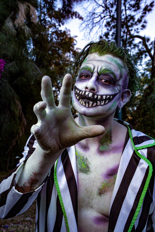 Free Spooky Halloween clown with face paint extends hand menacingly outdoors. Nighttime horror ambiance. Stock Photo