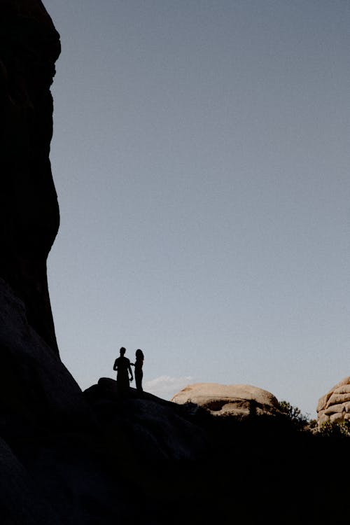 Silhouette of Two People Standing on Rock