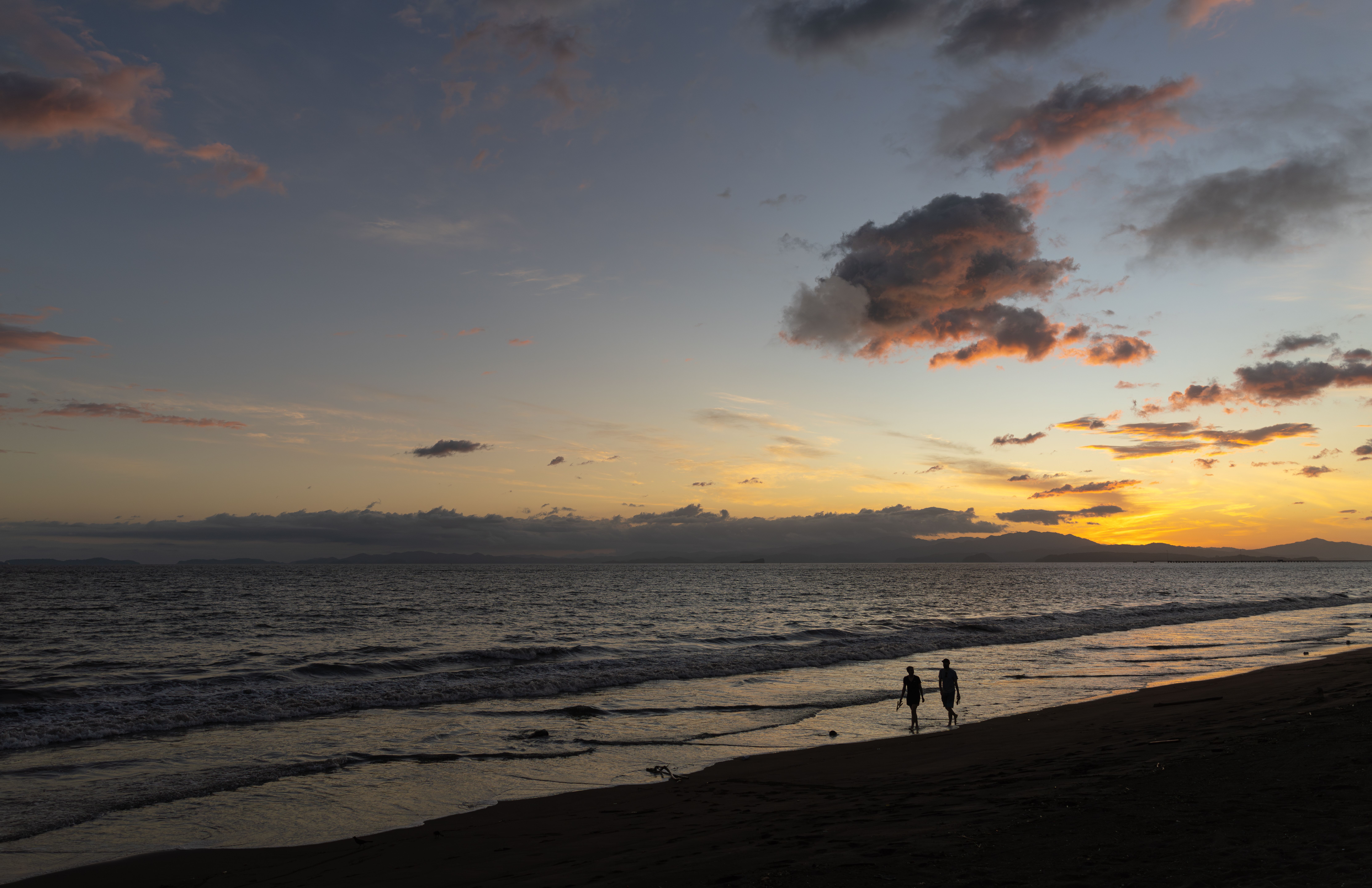 Romantic sunset view on Puntarenas beach with two people walking along the shore.