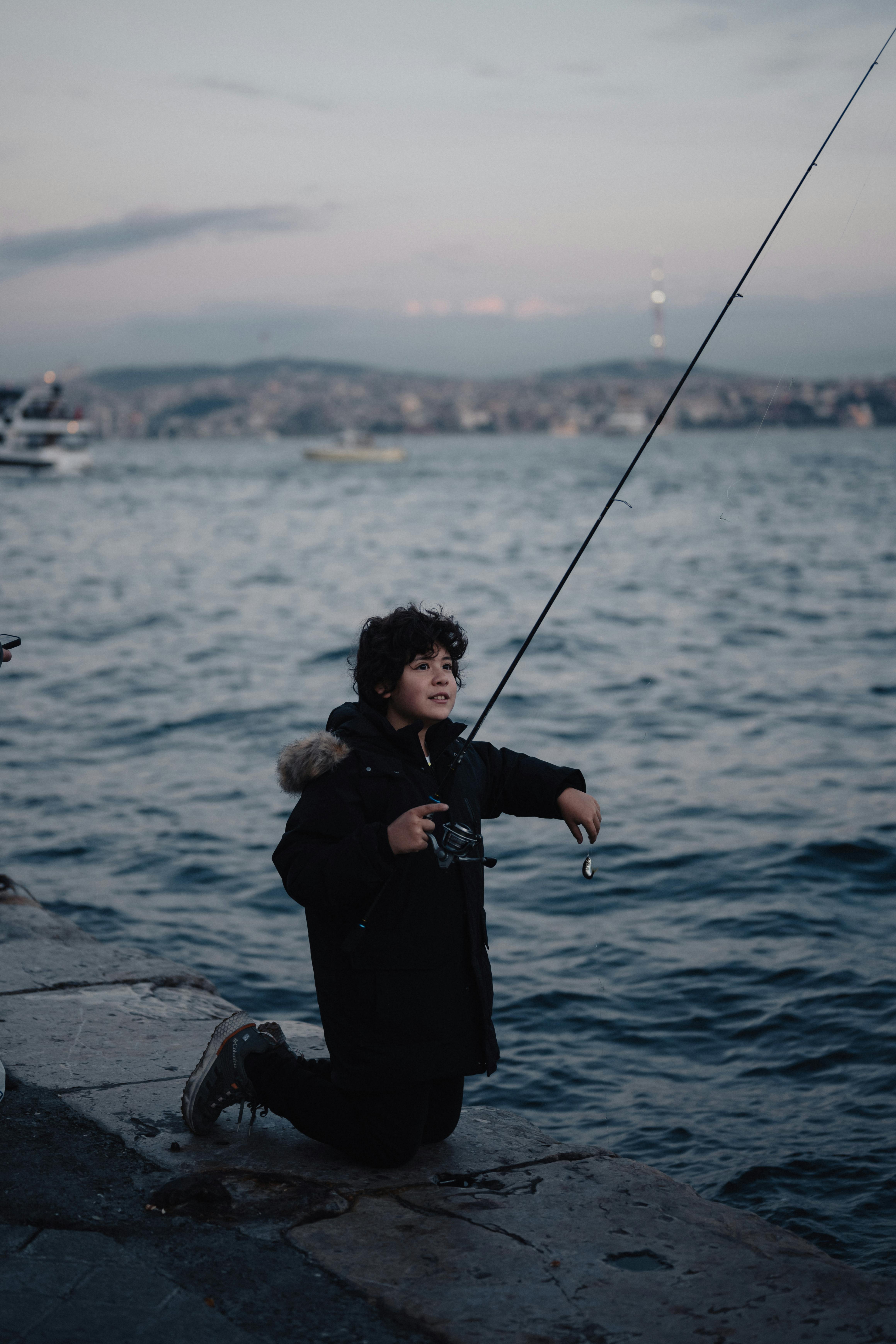 A child fishes by the Bosphorus at twilight in Istanbul, capturing a serene moment in the city.