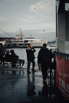 Candid scene of a fisherman in Istanbul, capturing the bustling life on the Bosphorus with boats and reflections on a rainy day.