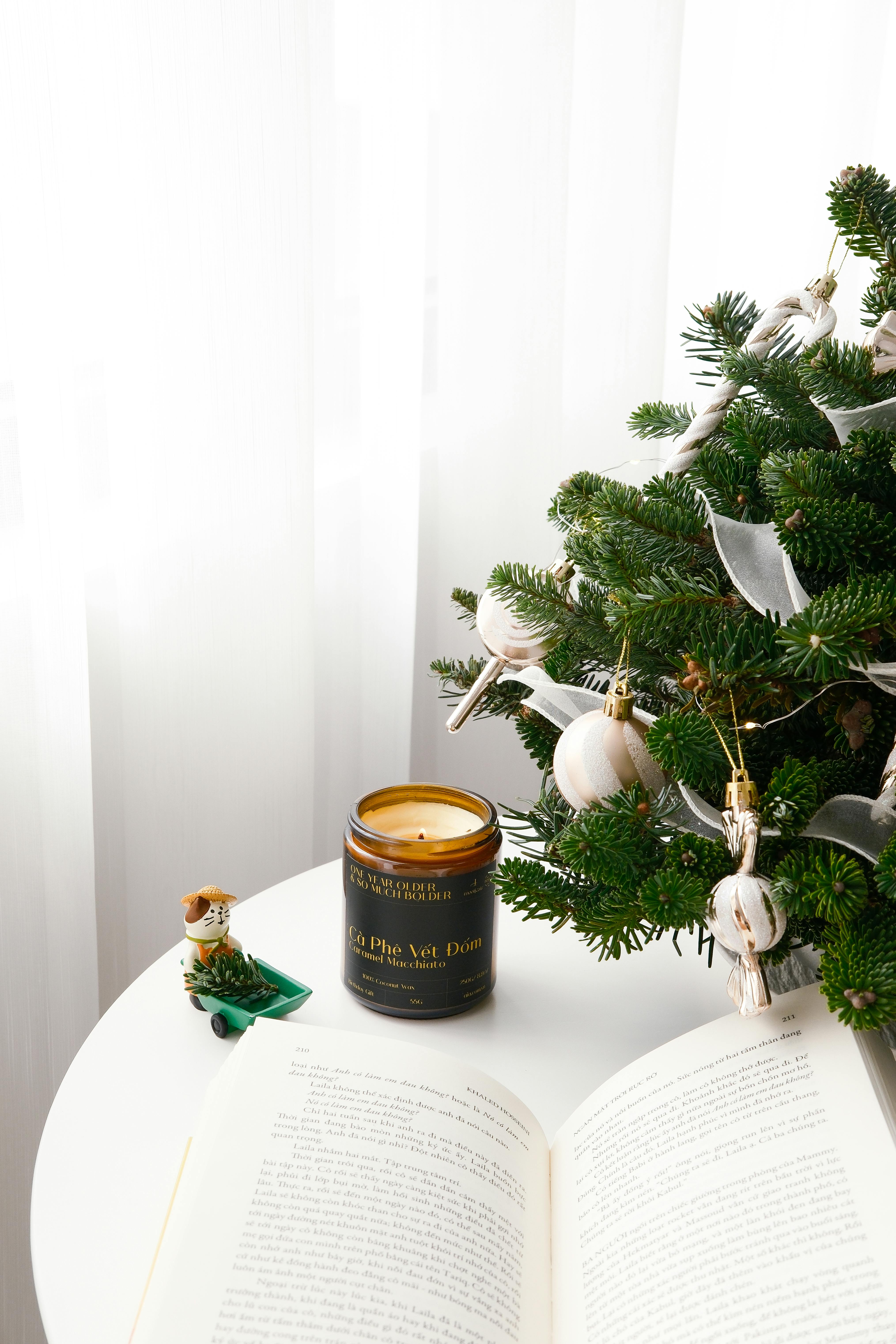 Festive candle beside a decorated fir tree on a round white table, capturing a holiday ambiance.