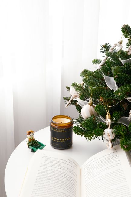 Festive candle beside a decorated fir tree on a round white table, capturing a holiday ambiance.