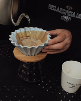 Close-up of artisan coffee brewing using a filter dripper, showing hands and precise technique.