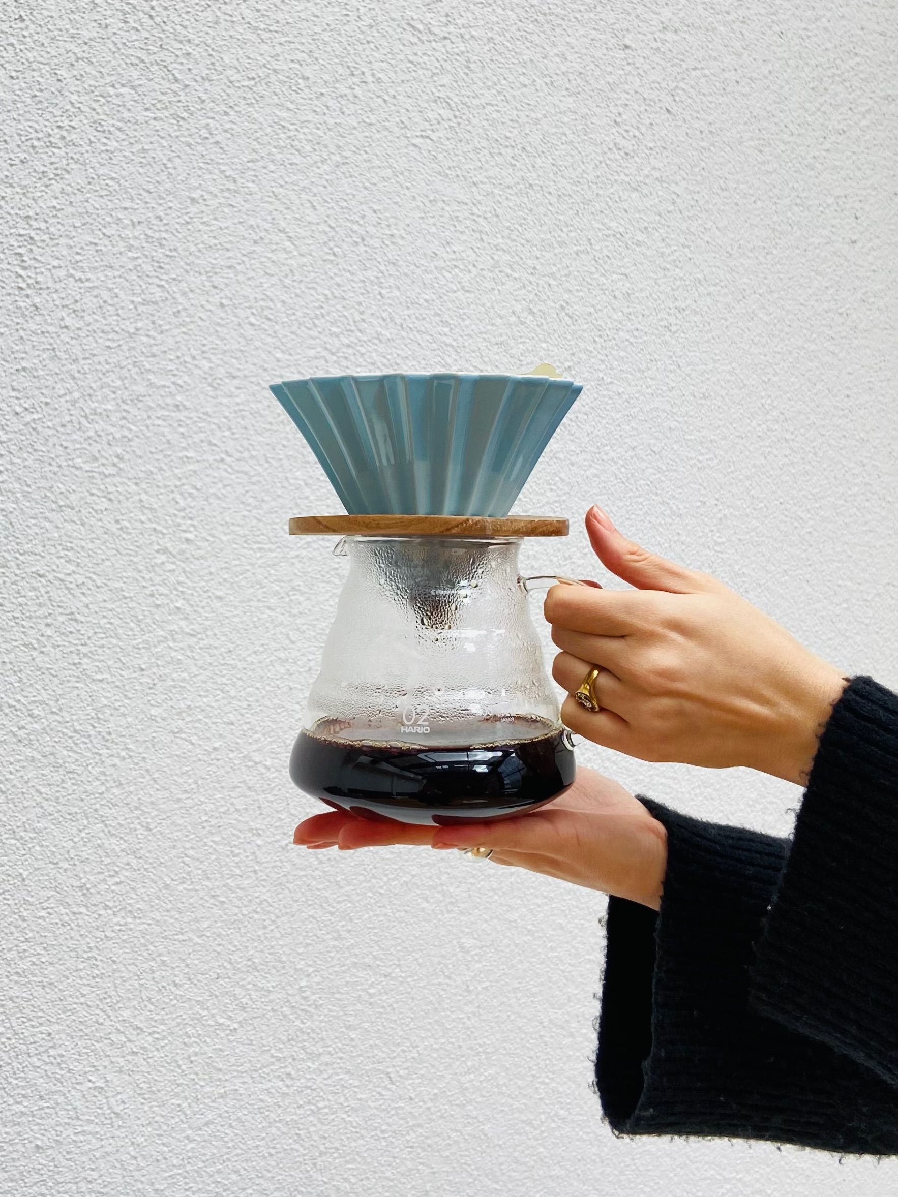 A close-up of a hand holding a glass pour-over coffee maker with ceramic filter.