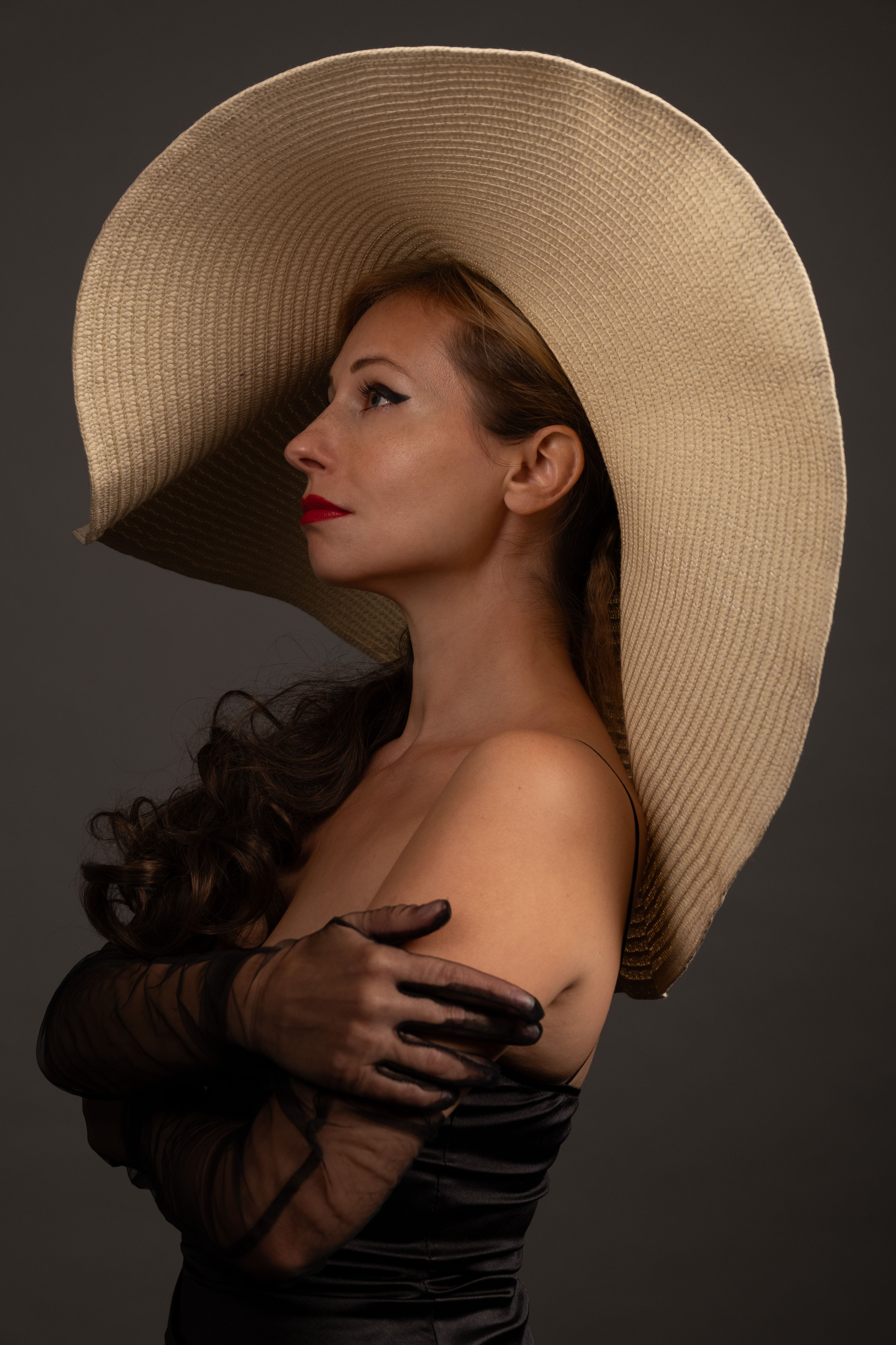 Sophisticated side profile of a woman with a wide-brimmed hat against a dark backdrop.