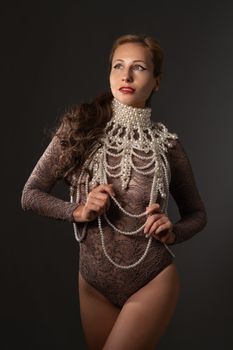 A sophisticated woman poses in a lace bodysuit adorned with an intricate pearl necklace.