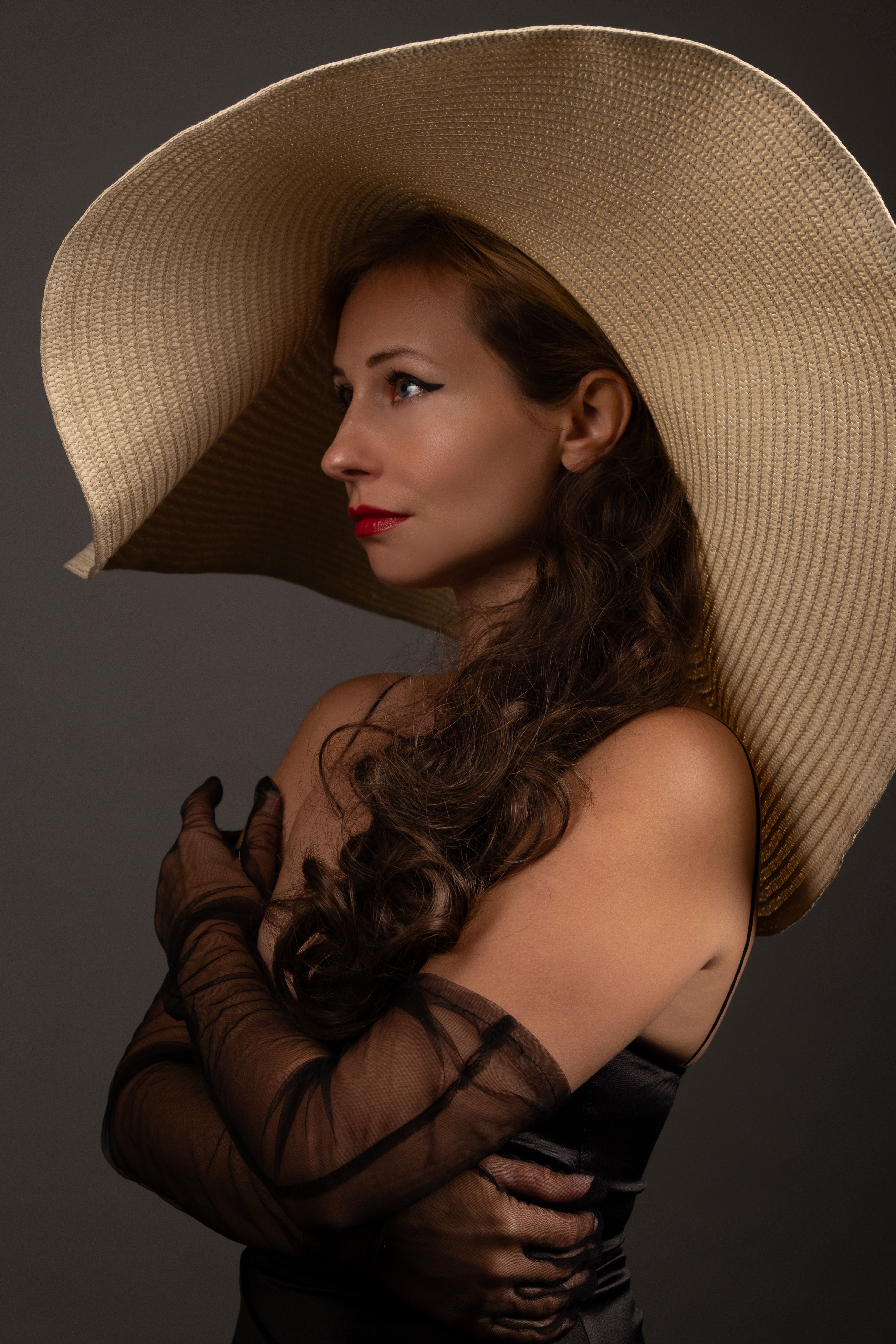 Side profile of a woman in a large elegant hat, wearing a black dress.