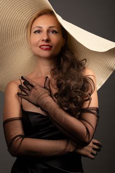 A stylish woman in black attire poses confidently with a wide-brimmed hat and sheer gloves.