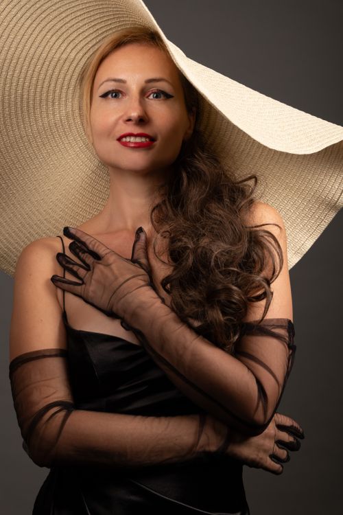 Free A stylish woman in black attire poses confidently with a wide-brimmed hat and sheer gloves. Stock Photo