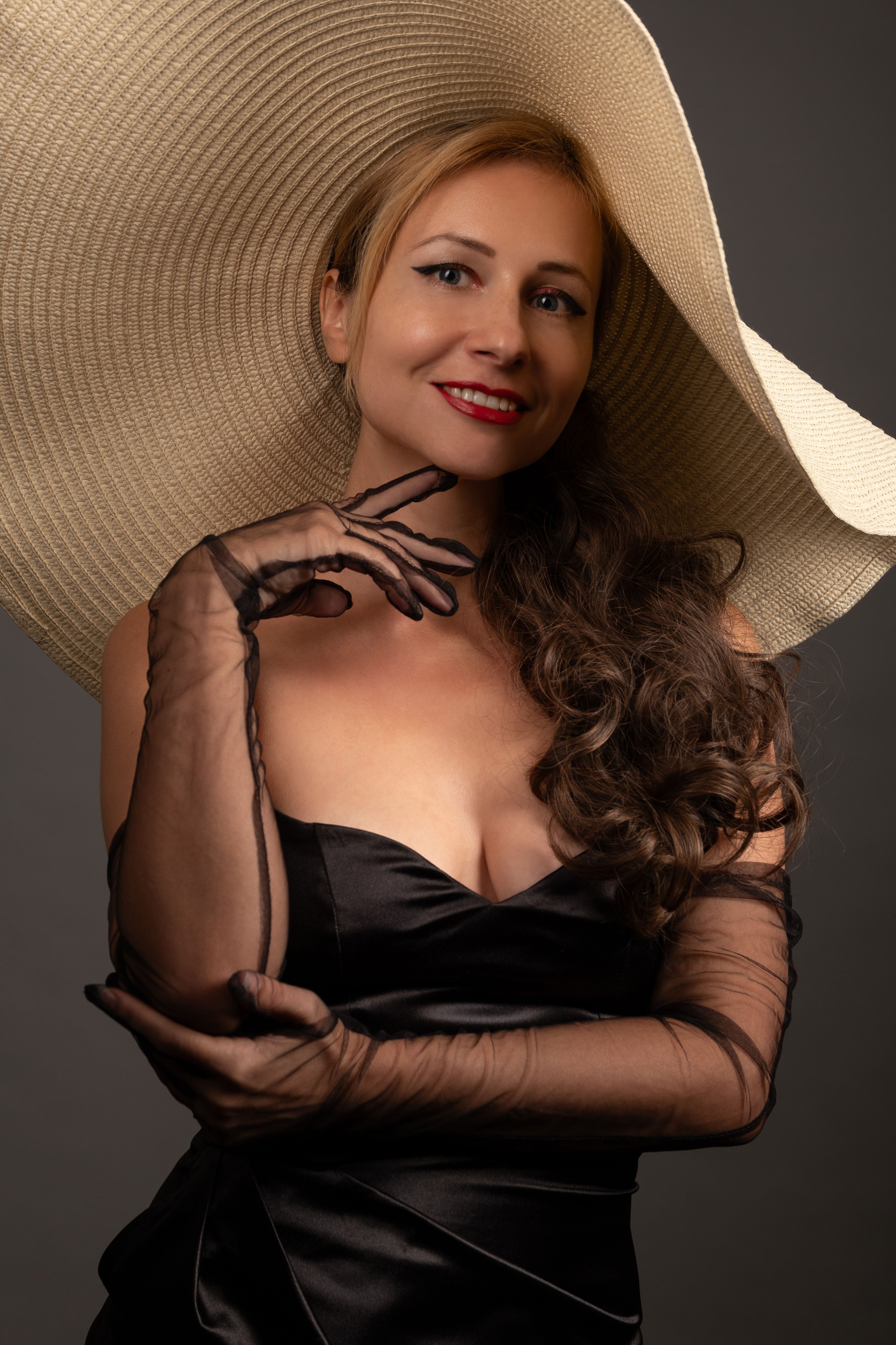 Stylish woman wearing a wide-brim hat and elegant black dress posing gracefully.