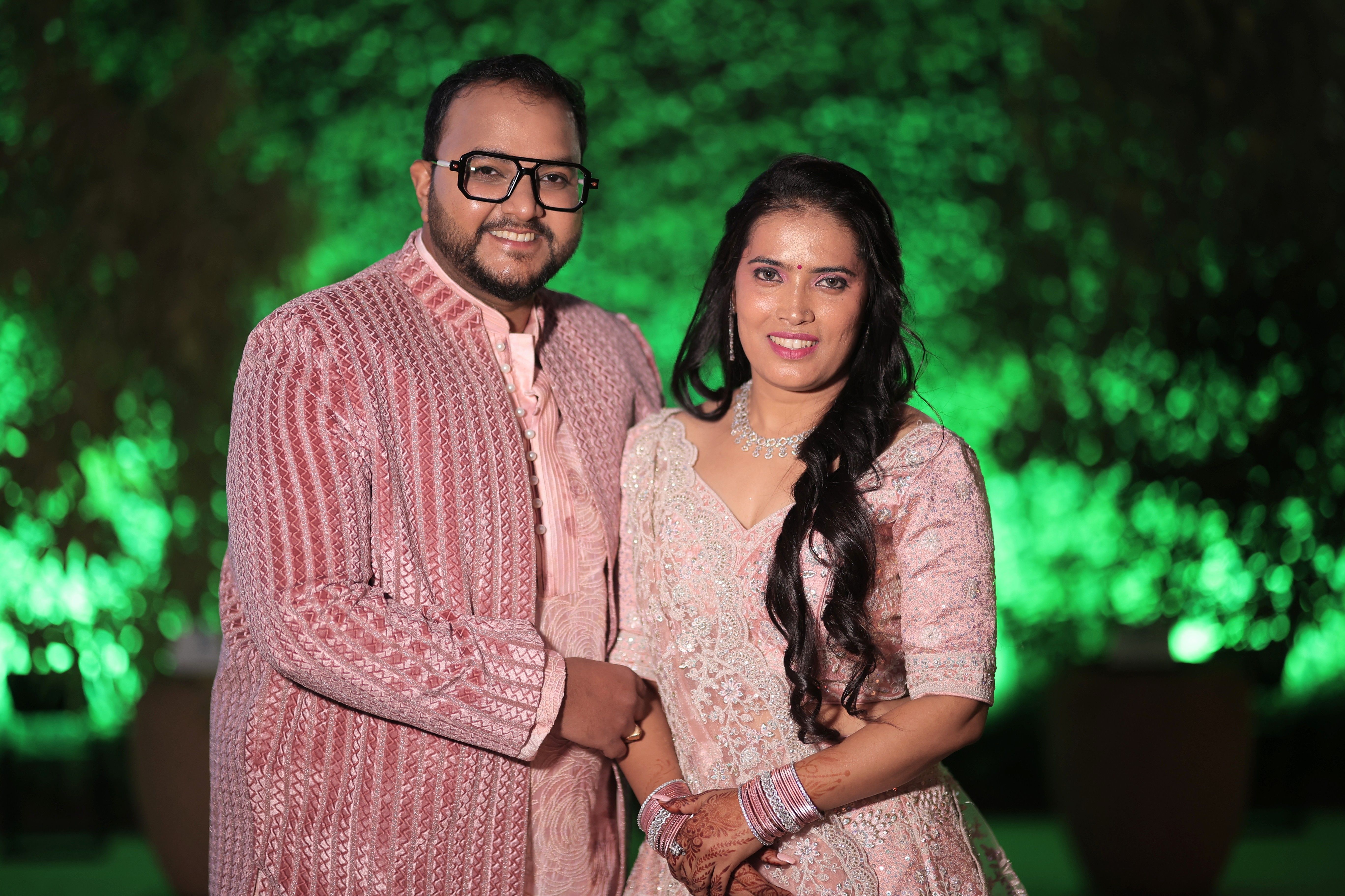 A beautifully dressed Indian couple posing indoors at a vibrant nighttime event.