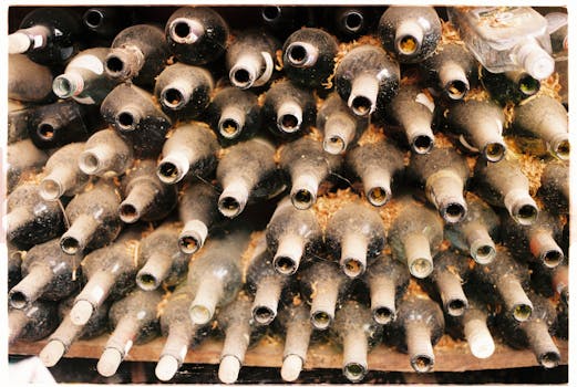 A collection of dusty, empty wine bottles stacked horizontally in an old cellar.