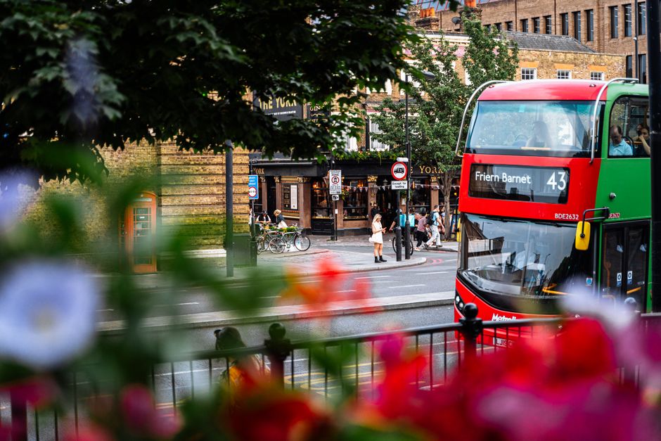 Red double-decker bus in vibrant London street scene with pedestrians and historic architecture.