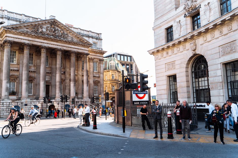 Bustling street scene at Bank Station, London with commuters, cyclists, and historic architecture.