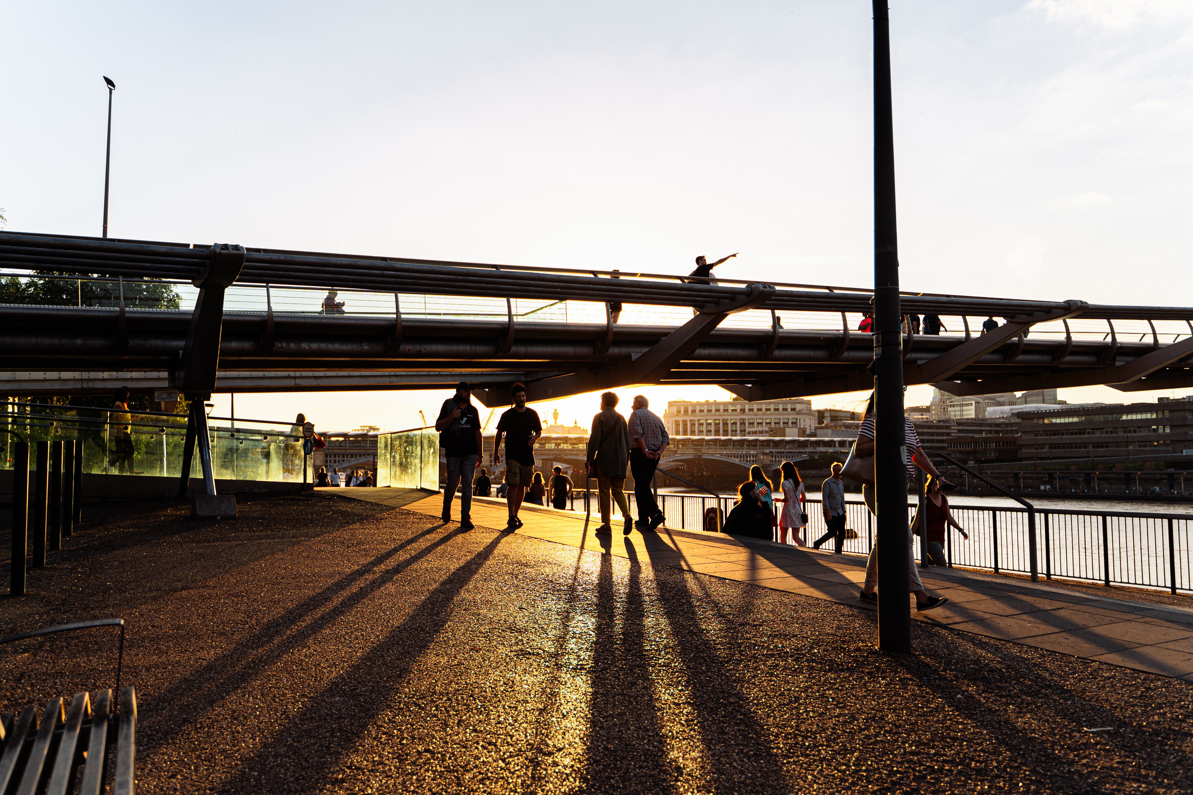 Silhouetted people walking on London's Millennium Bridge during a vibrant sunset.