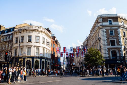 Free Crowded London street showcasing historic architecture and Union Jack flags under a clear sky. Stock Photo