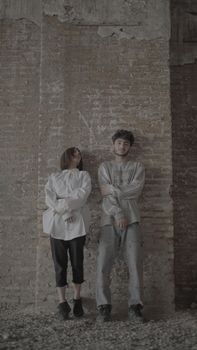 Two individuals standing against a brick wall in an urban setting. Casual fashion.