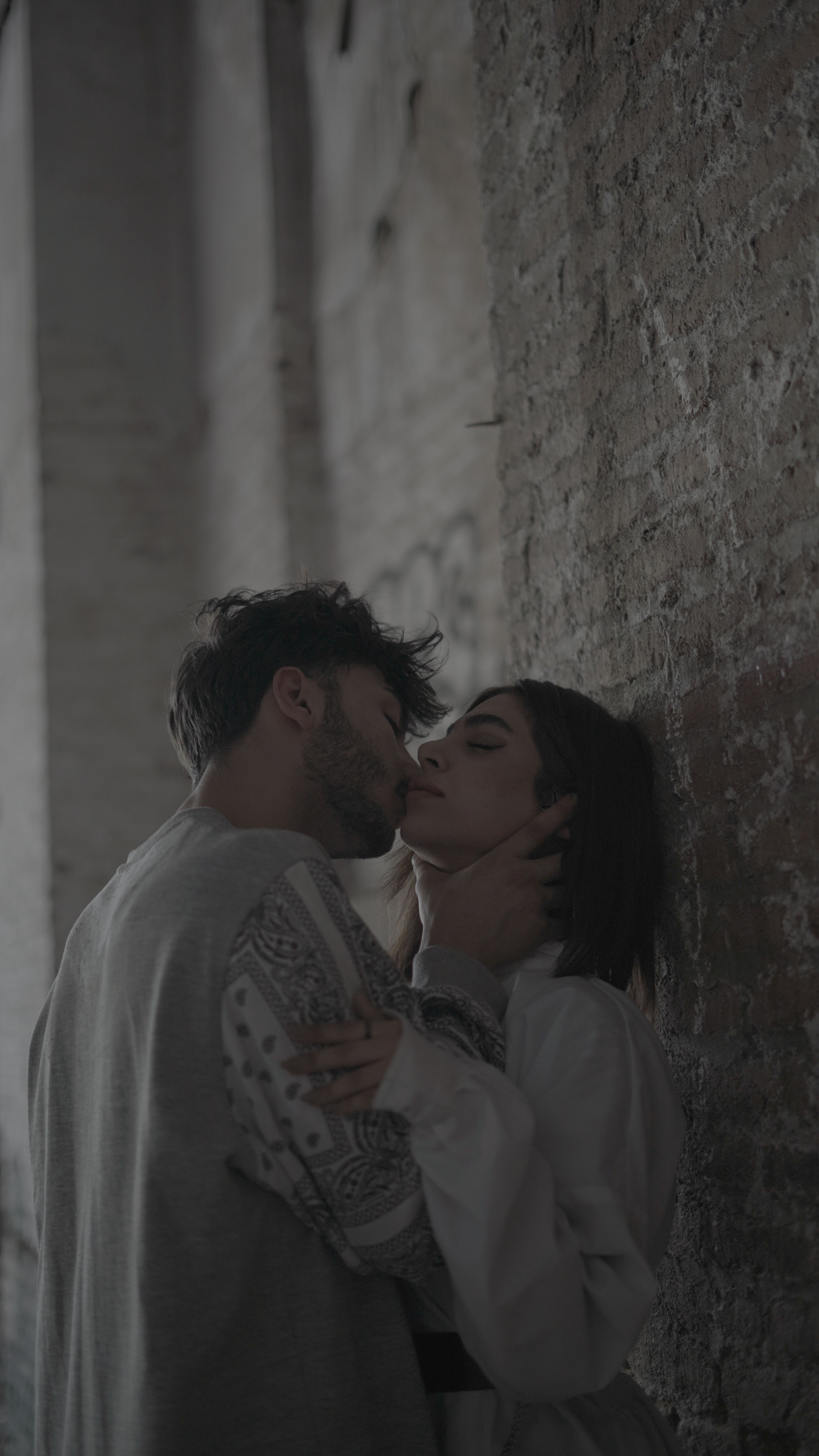 A romantic couple shares a tender kiss against a rustic wall.