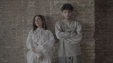 Young man and woman standing against a rustic brick wall, showcasing modern fashion and style.