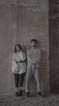 Two adults pose against a textured brick wall, showcasing modern casual fashion.
