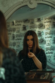 A woman applies lipstick while looking at her reflection in a vintage mirror.