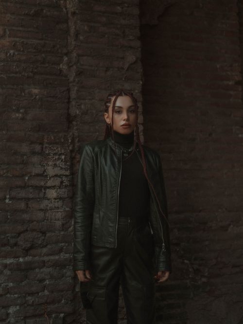 Free Fashionable young woman in leather jacket posing against rustic brick wall with dramatic lighting. Stock Photo