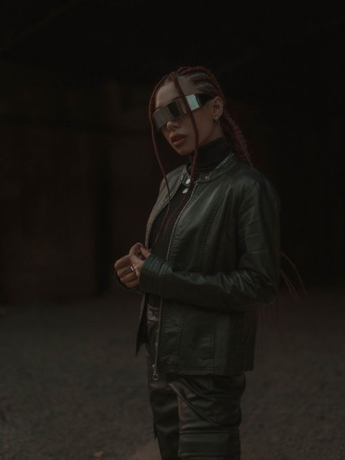 Free A fashionable woman wearing a leather jacket and futuristic glasses in a moody setting. Stock Photo