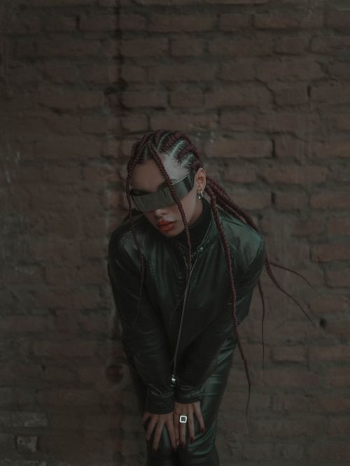 Free Fashionable woman wearing futuristic sunglasses and black leather leaning against a rustic brick wall. Stock Photo