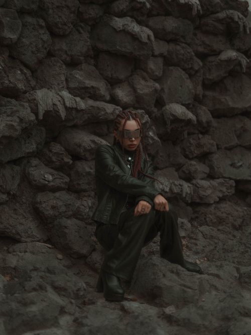 Free Dramatic portrait of a person with braided hair in a rocky setting, wearing sunglasses. Stock Photo