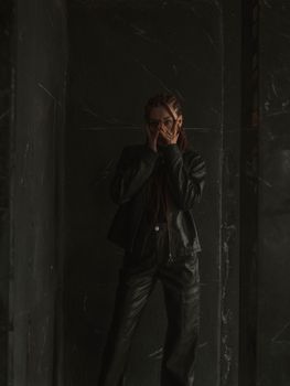 A person stands in a dark corner, wearing a leather outfit, evoking a mysterious and edgy vibe.