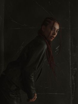 Moody portrait of a woman with braided hair in dark clothing posing indoors.