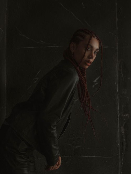 Free Moody portrait of a woman with braided hair in dark clothing posing indoors. Stock Photo